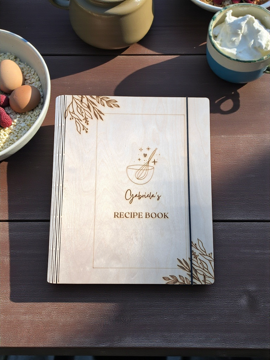 Recipe book with decorative cover on a wooden table with food items.
