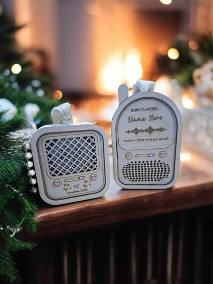 Two personalized Christmas radio ornaments displayed on a wooden mantel with a warm, blurred fireplace and holiday tree lights in the background.